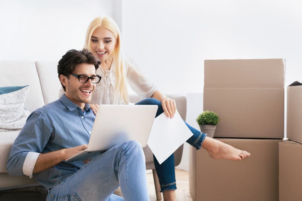 Couple unpacking boxes and browsing a laptop in their new home